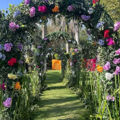 A magical garden entrance featuring a series of arches covered in lush greenery and colorful flowers, creating an enchanting tunnel for guests to walk through.