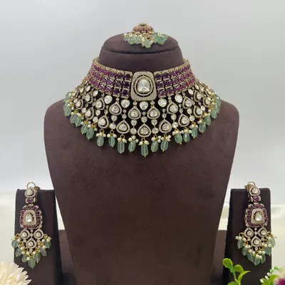The complete view of a premium bridal choker set. It features rows of ruby-colored stones, a layer of uncut polki, and mint-green bead drops, combining classic colors with a grand design. The set includes the choker, earrings, and maang tikka.