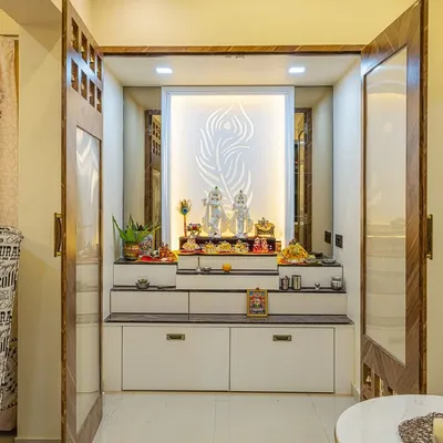 This is a custom-designed mandir with foldable doors. When open, it reveals a serene space with a backlit panel featuring a peacock feather motif, multi-level platforms for idols, and integrated drawers for storage.