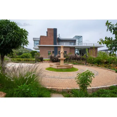 The grand entrance to our weekend home at Nandi Hills, featuring a circular driveway and a central water fountain. The landscape design uses native grasses and trees to frame the contemporary brick building, creating a welcoming approach.