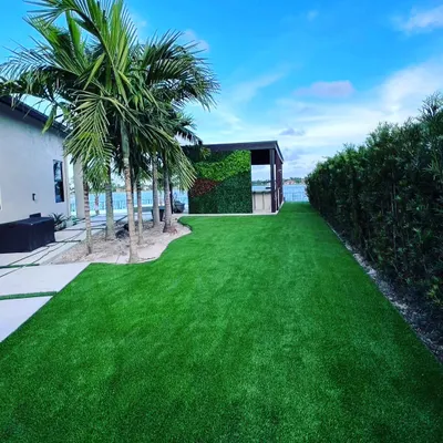 A large backyard with a complete artificial turf installation. The grass extends from the patio to a hedge and a separate cabana area, creating a seamless, clean green space.
