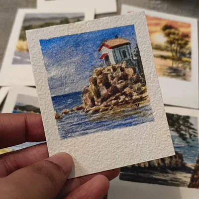 A miniature watercolor painting of a solitary lighthouse perched on a rocky cliff by the sea. The details in the stonework and the deep blue of the water make this a captivating little coastal scene.
