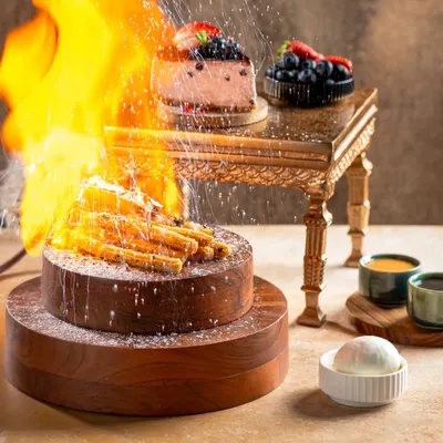 A dramatic shot of a flaming dessert at Bistro Flamme Bois, capturing the fire and powdered sugar shower for a theatrical dining experience.