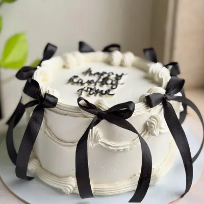 A full view of the balletcore-inspired cake, showcasing the classic piped swirls and the elegant arrangement of black satin bows around the sides and top.