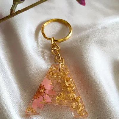 Initial keychains are a wonderful personalized gift. This 'A' keychain is made with light pink flower petals and shimmering gold flakes, creating a unique accessory that is handmade with love.