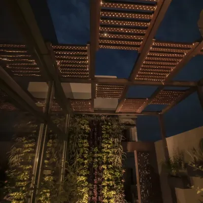 A stunning rooftop pergola at night. The integrated lighting within the Tipwood slats creates a warm, ambient glow, perfect for evening gatherings. The design is paired with a vertical garden wall.