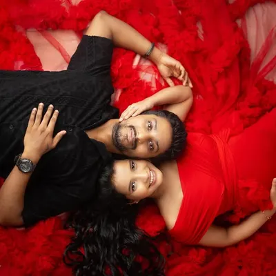 A little miracle is on the way. This overhead shot of an expecting couple, lying on a bed of vibrant red tulle, is a celebration of love and new life.