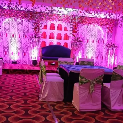We create stunning indoor settings for your special day. This stage setup for a wedding reception features intricate backdrop panels illuminated with vibrant pink uplighting, complemented by elegant white lounge seating for guests.