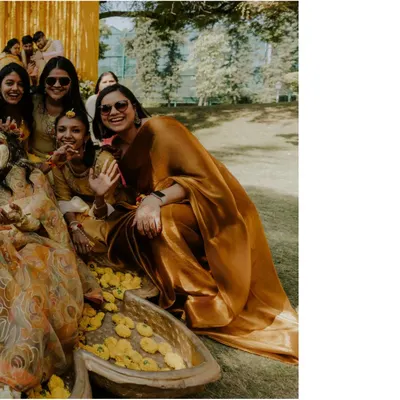 A candid shot of a wedding guest in a beautiful saree, smiling and waving, enjoying the outdoor Haldi ceremony.