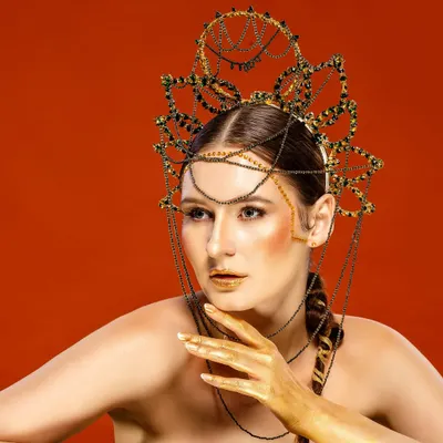 An editorial fashion portrait of an international model wearing an elaborate, artistic headpiece against a bold red background. This showcases our ability to execute high-concept, creative shoots for fashion magazines and campaigns.