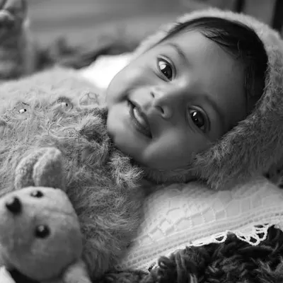 This black and white portrait of an awake baby in a teddy bear outfit is full of charm and personality. Monochrome tones highlight the baby's bright eyes and happy smile.