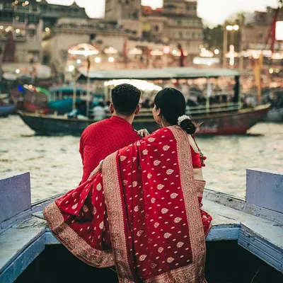 A wide shot from our Varanasi pre-wedding session, capturing the couple as they soak in the view of the ghats from their boat. The image establishes a sense of place, showing their shared moment against the vast, historic cityscape.