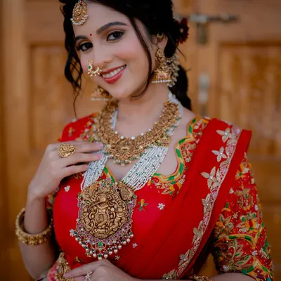 A radiant bridal portrait. The bride's joyful smile and the stunning details of her red half saree and temple jewellery are captured perfectly in the soft, natural light.