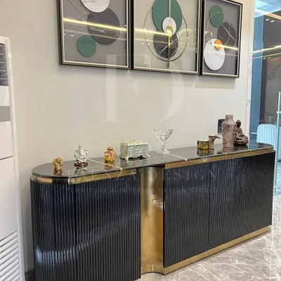 This modern console unit is a statement piece, featuring a fluted black wood finish, a black marble top, and a striking asymmetrical design with a polished gold-finished accent.