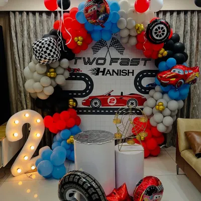A "Two Fast" racing car theme for a second birthday. This setup includes a custom backdrop with a racetrack, a circular balloon arch in red, black, and white, and a large light-up number '2'.