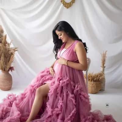 A quiet moment of reflection for this beautiful mama-to-be, seated in a stunning ruffled pink gown that fills the frame with color and texture.