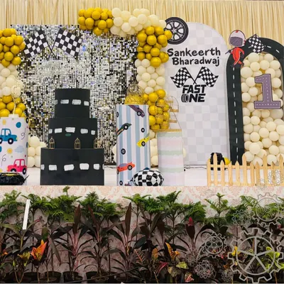 A full view of the "Fast One" racetrack-themed first birthday party. The setup includes a custom cake table, a backdrop with road graphics, and balloon arrangements, creating a fun and dynamic environment for the celebration.