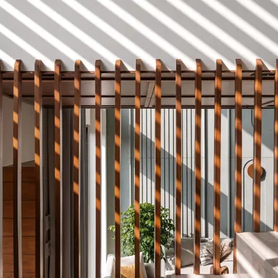 The play of light and shadow is a key element in our designs. In Amber House, the afternoon sun streams through the vertical wooden railings, casting graphic patterns on the walls and floor, transforming the architectural structure into a living piece of art.