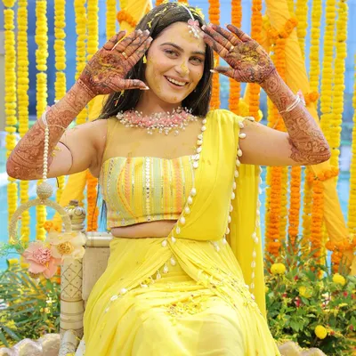 A joyful bride shows off her intricate henna designs during her Haldi ceremony. Her bright smile and the vibrant yellow decor create a picture of pure happiness and anticipation.