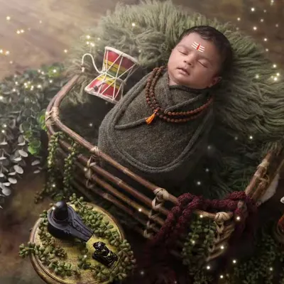 A powerful and serene portrait of a newborn as little Mahadev. This overhead shot captures the full divine setup, including the Shivling, Trishul, and Rudraksha beads.