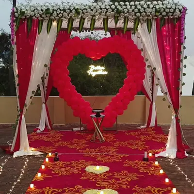 A perfect proposal setup on a rooftop, complete with a red carpet, candle-lit pathway, and a large heart-shaped balloon arch framing a 'Better Together' neon sign.