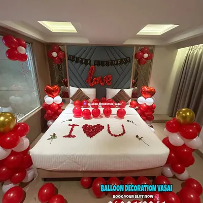 A classic romantic room decoration in red and white. The setup includes balloon pillars, a "love" foil balloon, and "I ❤️ U" written with rose petals on the bed.