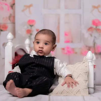 A classic portrait of a 4-month-old baby boy sitting up on the prop bed. His alert expression and formal outfit make for a very handsome photo.