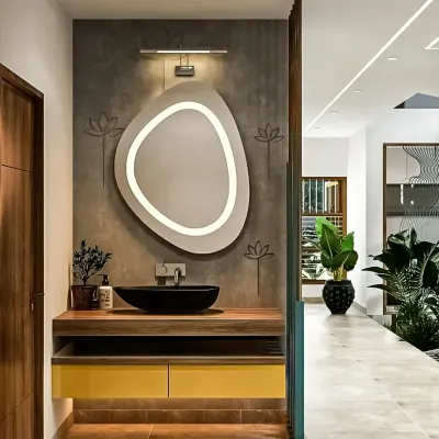 A chic washbasin area featuring a unique, organically shaped backlit mirror. The floating wooden vanity with a black vessel sink and yellow drawers adds a pop of color and modern flair.