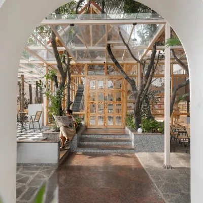 The entrance to the Bake House, framed by a traditional archway. The view reveals a glass-and-wood pavilion built carefully around existing trees, immediately establishing the project's nature-centric theme.