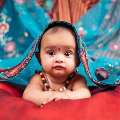 A stunning close-up of a 6-month-old baby, peeking from under a vibrant blue dupatta. A beautiful blend of tradition and cuteness.