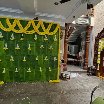 For an intimate home ceremony, we created this backdrop entirely from fresh banana leaves. The wall is decorated with small pendants made of jasmine and marigold flowers, creating a completely natural and traditional look.