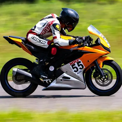 A side profile view of a rider executing a turn, demonstrating the correct tucked-in body posture to minimize drag and maintain stability at speed. This is a fundamental aspect of our motorcycle race training.