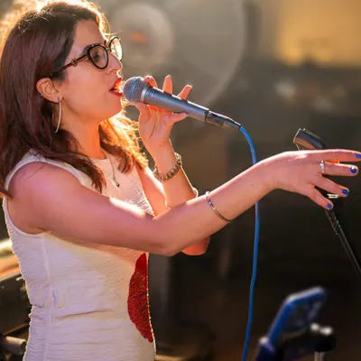 I'm reaching towards the audience while singing into a handheld mic, with warm light catching my hair on stage.