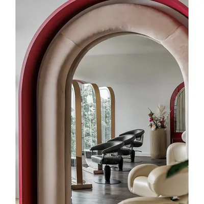 A view through a series of plush, velvet-lined arches reveals the salon's styling stations. This architectural feature creates a sense of drama and discovery, guiding clients through the space while offering glimpses of what lies beyond.