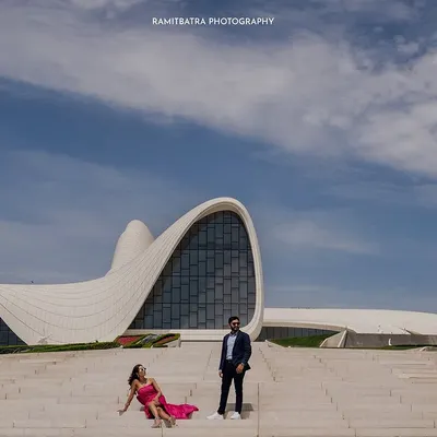 A stunning wide-angle shot of the couple posing at the Heydar Aliyev Centre in Baku, its futuristic curves contrasting with the blue sky.