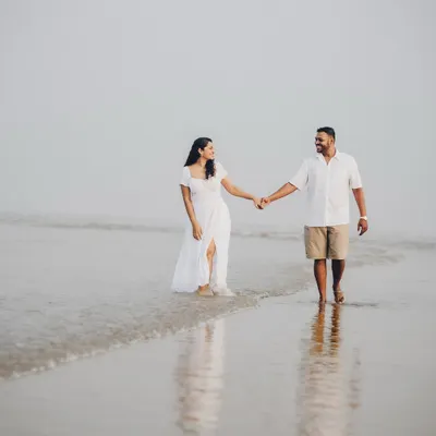 Janice and Lyle walking hand-in-hand during their misty morning beach session. The soft light and reflections on the wet sand create a dreamy, ethereal quality.