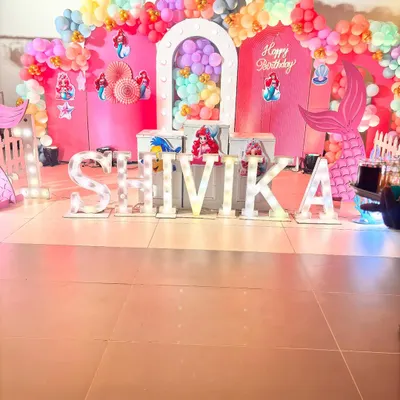 This is a complete stage setup for a Little Mermaid theme party. I used a vibrant pink backdrop, a colorful balloon arch, and large marquee letters, along with multiple cutouts of Ariel and her friends to create a lively underwater scene.