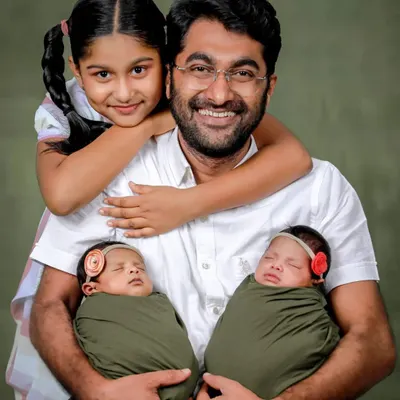 A proud father with his three children, holding his newborn twins while his older daughter gives him a hug. A heartwarming studio portrait of a growing family.