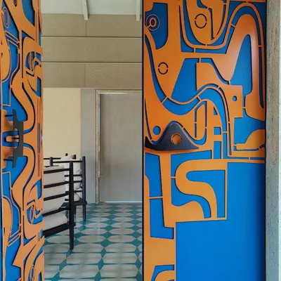 A close-up view of our custom-designed metal door, showcasing the layered mild steel construction and the unique, hand-sculpted handles. The vibrant contrast between the orange and blue creates a powerful visual impact.