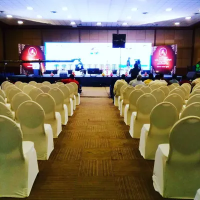 This is a view from the back of a conference hall before the event begins, showcasing a clean and organized seating arrangement. I ensure every detail is in place, from chair covers to the main stage setup, for a professional look.