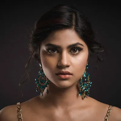 A captivating studio headshot for a model's portfolio. The clean, dark background and professional lighting put the full focus on her direct gaze and the elegant statement earrings.