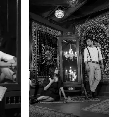 A moody black and white portrait from a stylized indoor shoot. The intricate set design, with carpets and a chandelier reflection, creates a rich, vintage, and dramatic atmosphere.