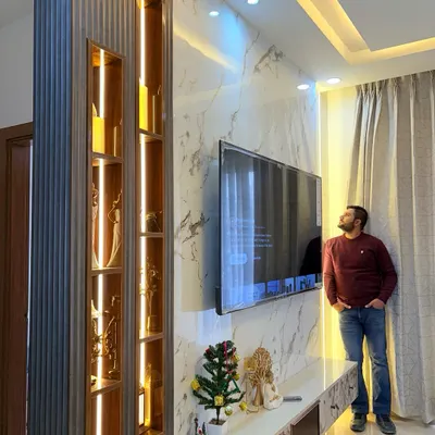 Admiring a finished TV unit. This design features a marble-finish back panel, a fluted wood partition with illuminated display niches, and a sleek console, creating a stunning centerpiece for the living room.