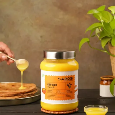 A lifestyle shot showing A2 Cow Ghee being drizzled onto a stack of parathas. This image demonstrates the product in use, making it instantly relatable and desirable for a home kitchen.