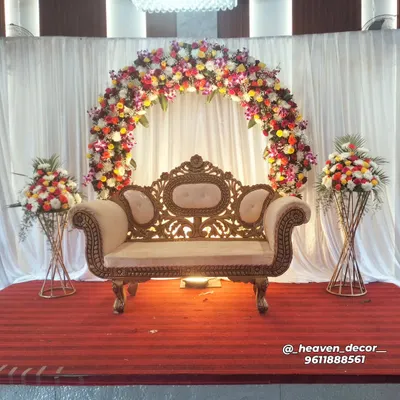 A classic and beautiful full floral arch provides a timeless backdrop for any reception or engagement. The mix of colorful flowers creates a vibrant and celebratory focal point, complemented by an ornate, traditional sofa.