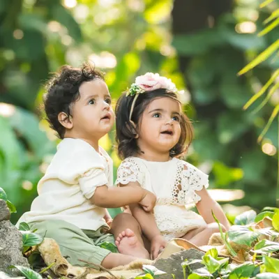Two little explorers. These adorable twins, a boy and a girl, look up in wonder during their outdoor photoshoot, their bond clear to see.