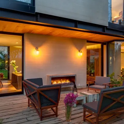 This backyard patio is designed as an extension of the home's living space. It features our custom-designed rustic wooden lounge furniture arranged around a modern outdoor fireplace, creating an inviting area for relaxation and entertaining.