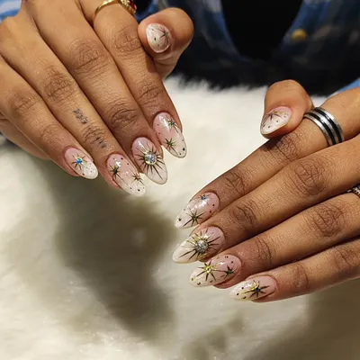 A celestial dream on your fingertips. This stunning set features a soft white ombre base on almond nails, decorated with intricate golden starbursts, tiny gold dots, and sparkling rhinestone centers.