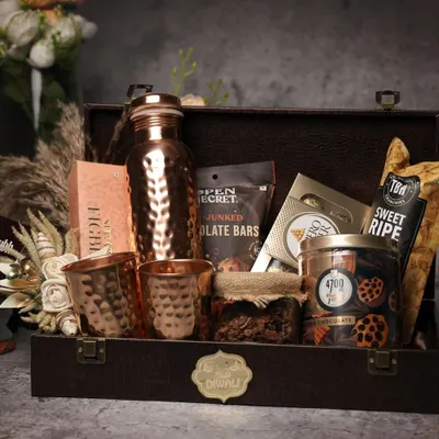 A classic Diwali hamper featuring a hammered copper bottle and glasses, packed in a rustic leather-finish trunk. This gift combines traditional wellness with modern aesthetics, filled with gourmet snacks and treats.