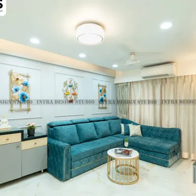 We designed this spacious living room with a comfortable teal L-shaped sofa, perfect for family gatherings. The light grey feature wall with classic moulding and artistic decor adds a touch of elegance and personality.